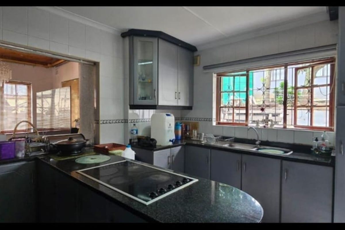 Functional kitchen featuring dark granite countertops, built-in electric hob, ample cabinetry, and a large window providing natural light and a view to the exterior.
