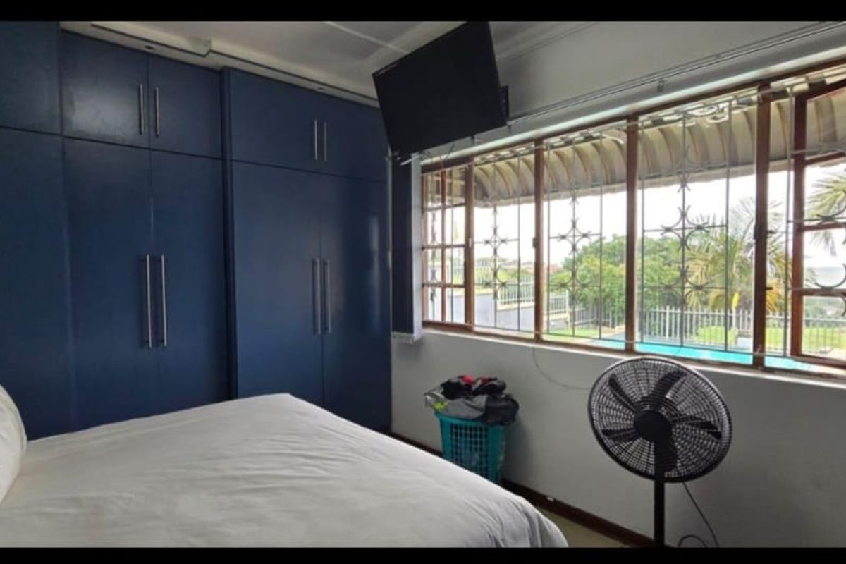 A bedroom featuring extensive floor-to-ceiling built-in cabinetry and large windows with security bars, offering a view of the outdoor pool area.