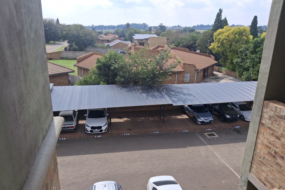 Elevated view overlooking the apartment complex parking area, featuring covered carports with corrugated metal roofing and paved parking bays.