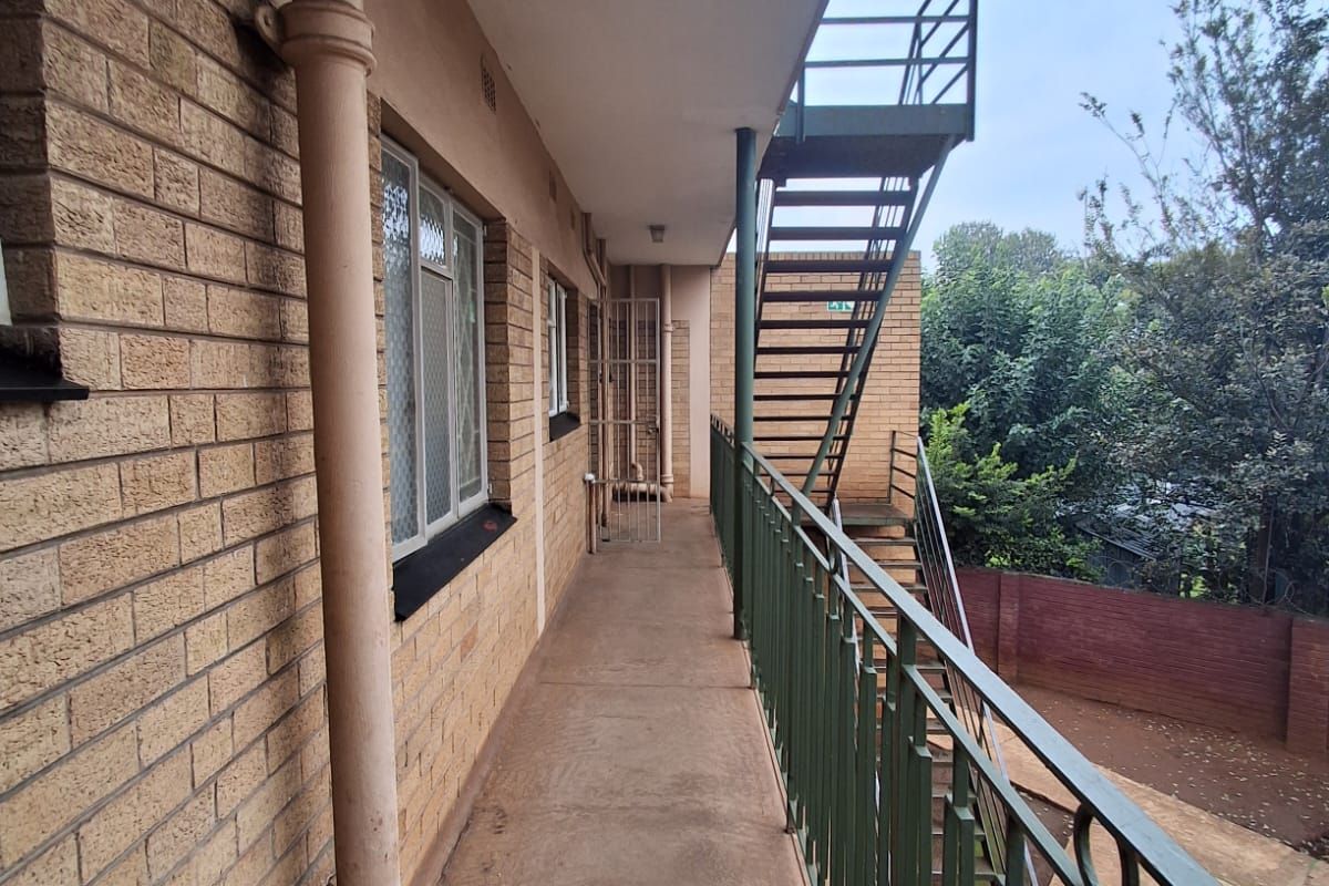 Exterior walkway and fire escape staircase providing access to the flat, featuring brick facade and metal safety railings.