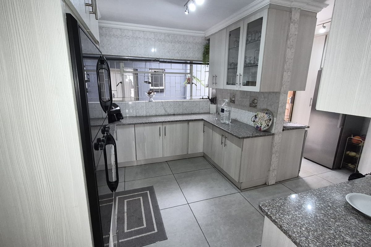 A functional kitchen featuring light-toned cabinetry, granite countertops, tiled backsplash, and large floor tiles, offering a clean and practical workspace.