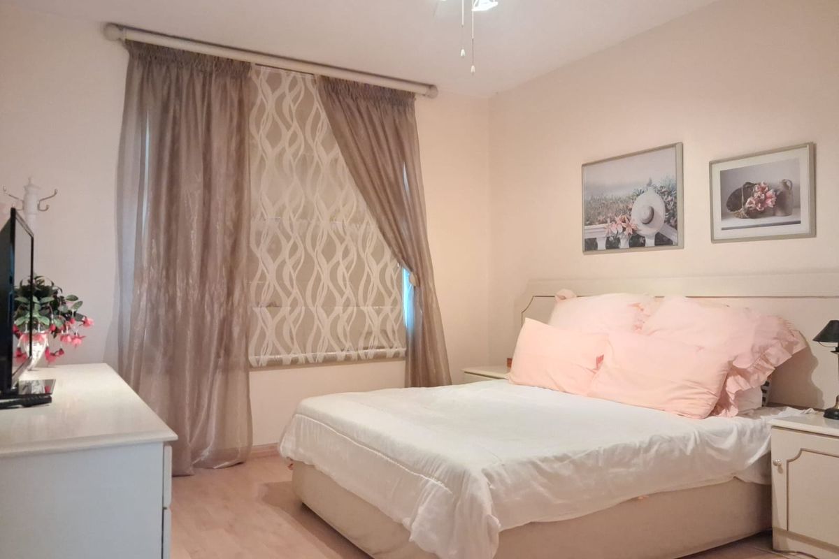 A well-lit bedroom featuring light-toned laminate flooring, neutral wall finishes, and a ceiling fan with integrated lighting.