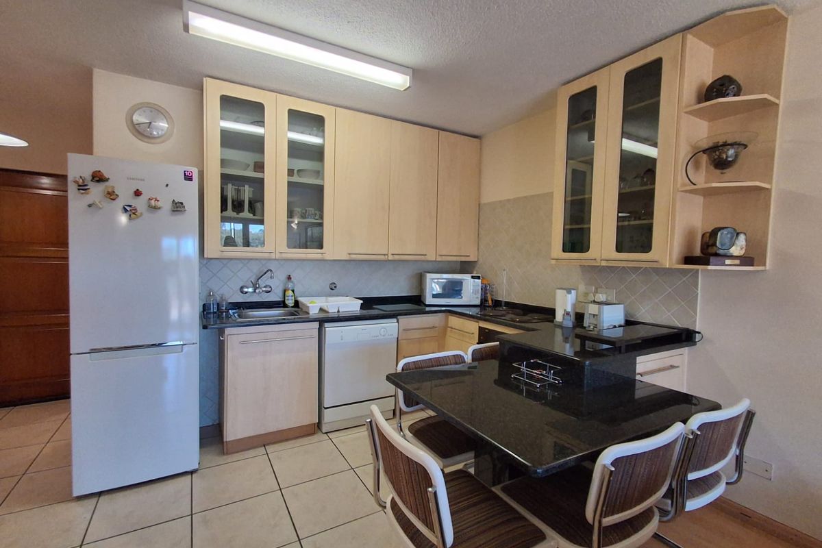 A functional kitchen featuring light wood cabinetry, dark granite countertops, a breakfast bar, and tiled flooring.