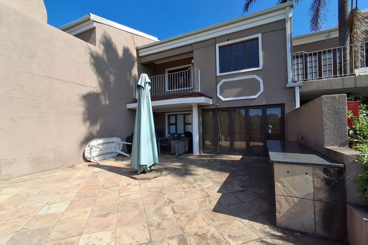 Rear exterior view of the townhouse featuring a paved patio area, built-in stone counter, and a covered balcony on the upper level.