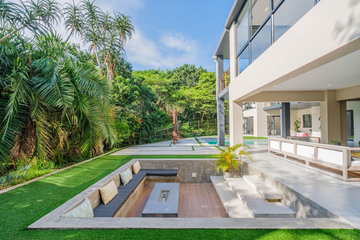 Modern rear exterior featuring a sunken fire pit area, tiled patio, swimming pool, and landscaped garden with lush greenery.