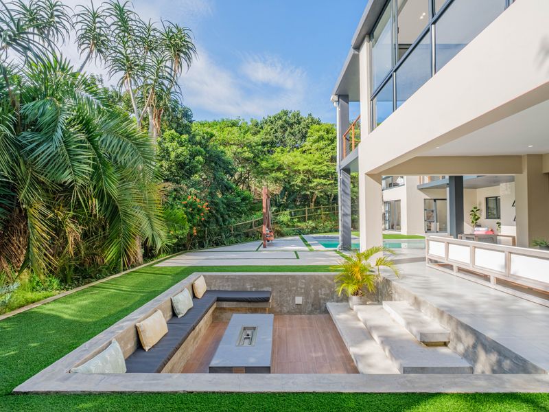 Modern rear exterior featuring a sunken fire pit area, tiled patio, swimming pool, and landscaped garden with lush greenery.