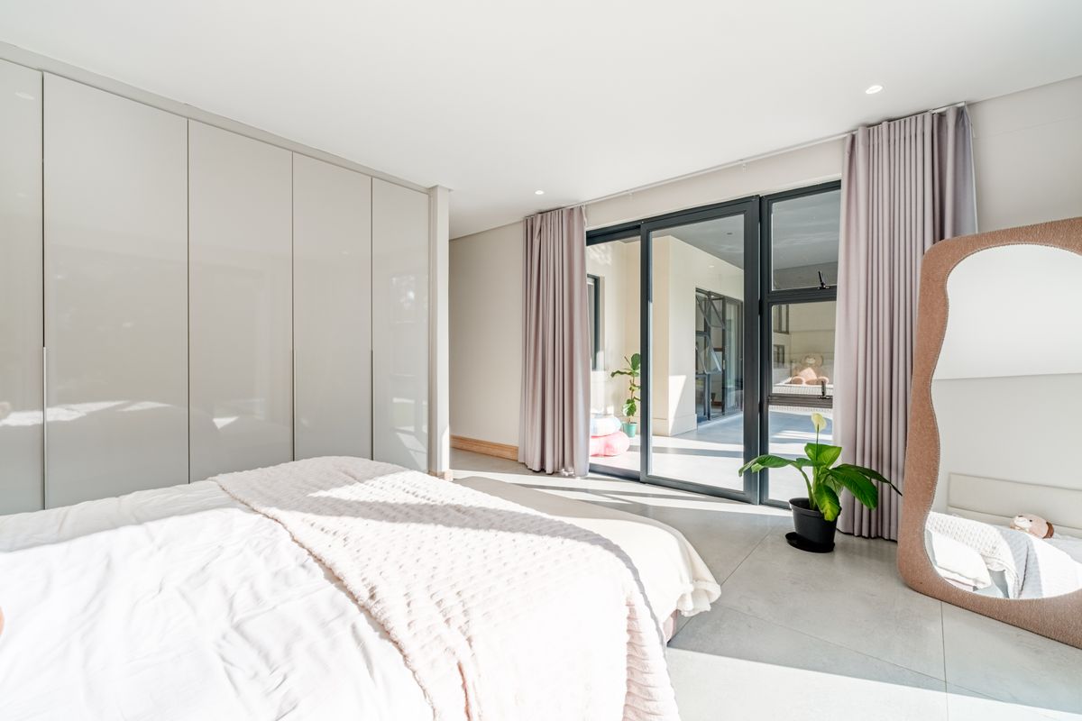 Modern bedroom featuring sleek built-in cupboards, large sliding glass doors leading to a patio, and neutral tiled flooring with recessed lighting.