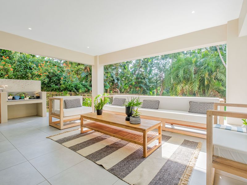 A spacious covered patio featuring tiled flooring, recessed lighting, and a built-in braai area, overlooking a lush garden.