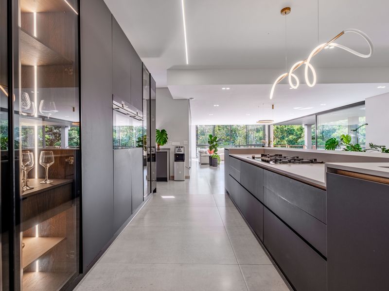 Modern, high-end kitchen featuring sleek dark cabinetry, integrated appliances, a central island with a gas hob, and premium stone countertops.