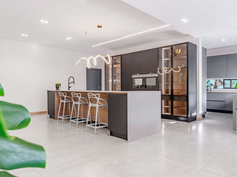 Modern kitchen featuring a large central island, sleek dark cabinetry, integrated appliances, and high-end glass display units with recessed lighting.