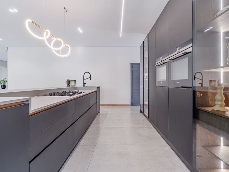 Modern, high-end kitchen featuring sleek dark cabinetry, integrated appliances, stone countertops, and a gas hob, complemented by contemporary lighting and large-format floor tiles.