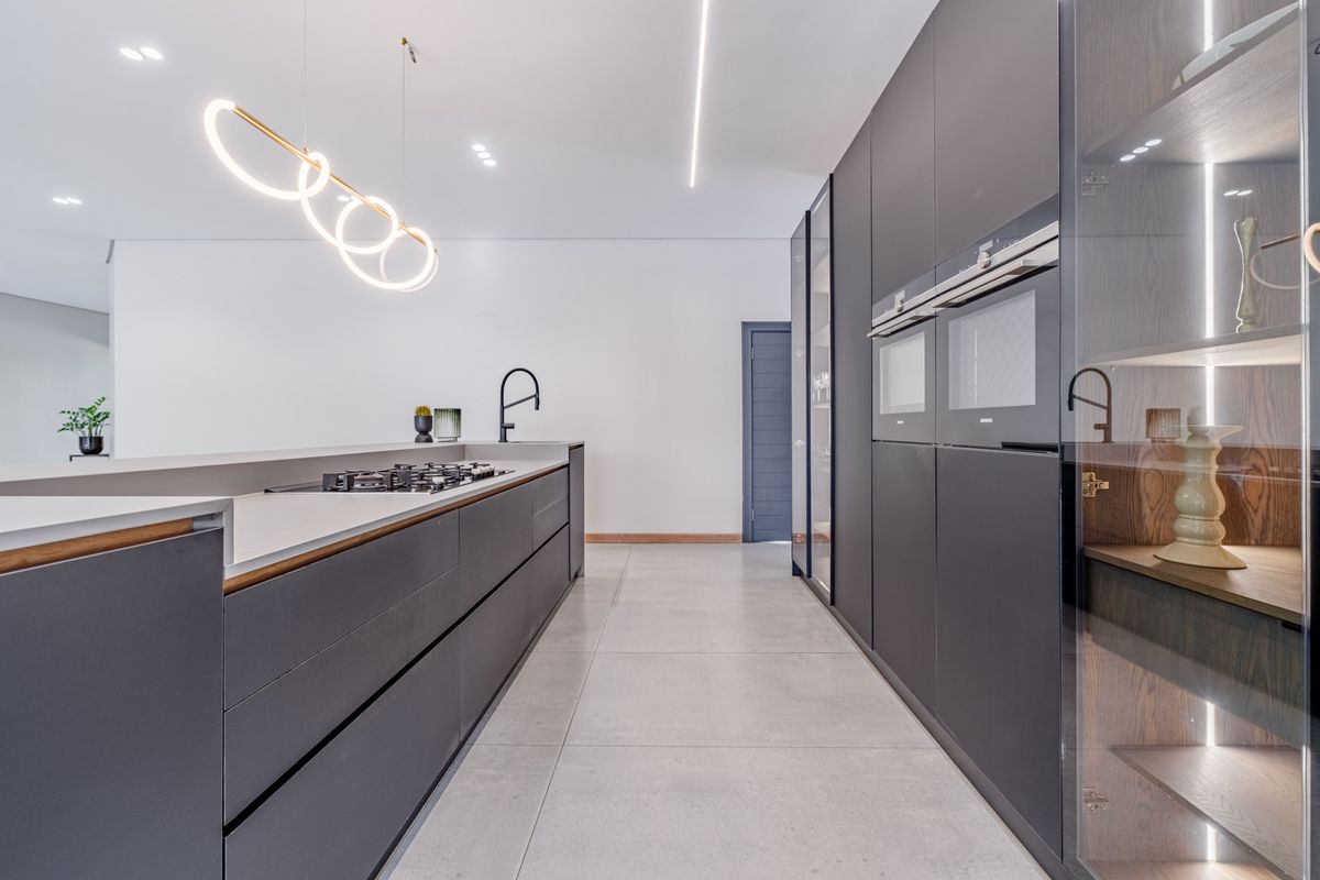 Modern, high-end kitchen featuring sleek dark cabinetry, integrated appliances, stone countertops, and a gas hob, complemented by contemporary lighting and large-format floor tiles.