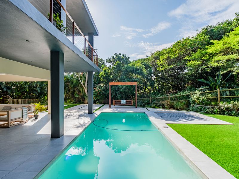 A modern outdoor living space featuring a swimming pool, covered patio area, and landscaped garden with artificial turf.