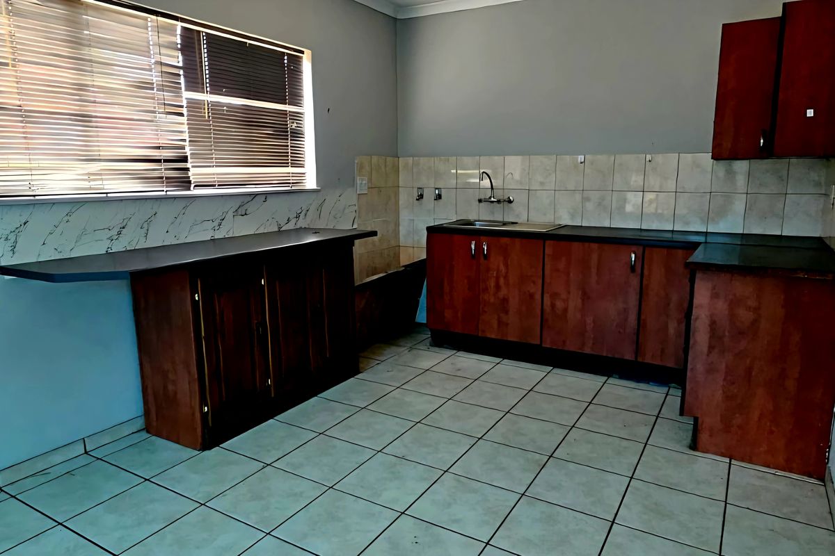 A functional kitchen featuring wooden cabinetry, tiled splashbacks, a stainless steel sink, and tiled flooring, offering a practical layout for daily meal preparation.