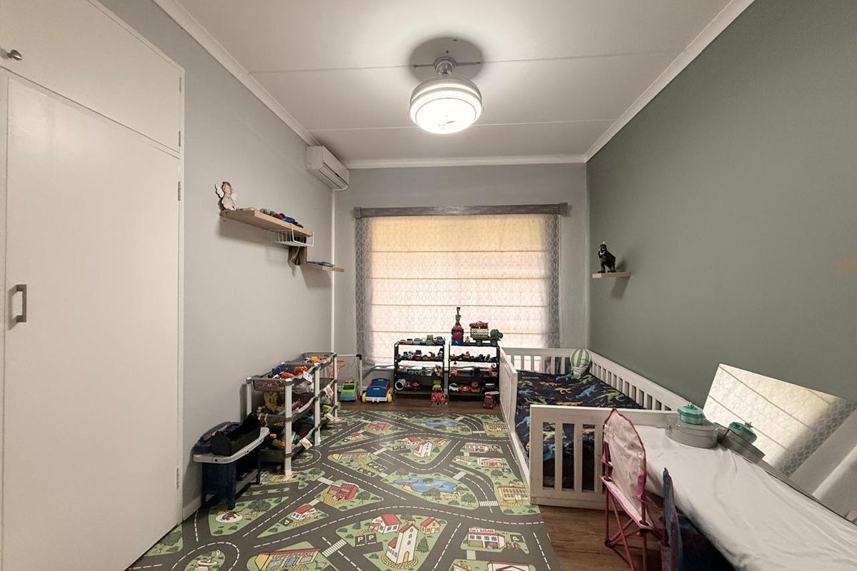 A bedroom featuring wood-look flooring, a built-in cupboard, a wall-mounted air conditioning unit, and a central ceiling light fixture.
