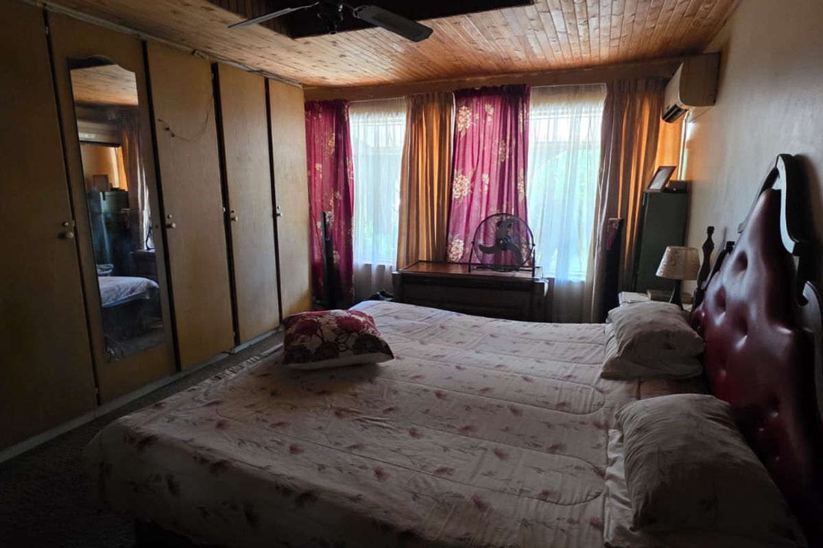 A bedroom featuring built-in wooden wardrobes, a timber-clad ceiling, and large windows with curtains.