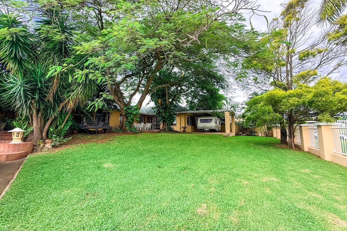 A spacious rear garden featuring a well-maintained lawn, mature trees, and a covered carport area attached to the main house.