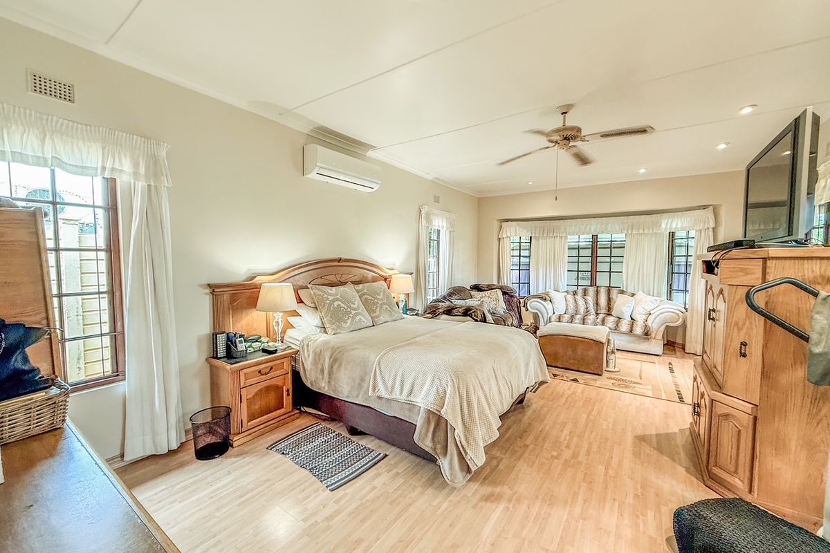 Spacious bedroom featuring laminate flooring, a ceiling fan, and a wall-mounted air conditioning unit, with large windows providing natural light.