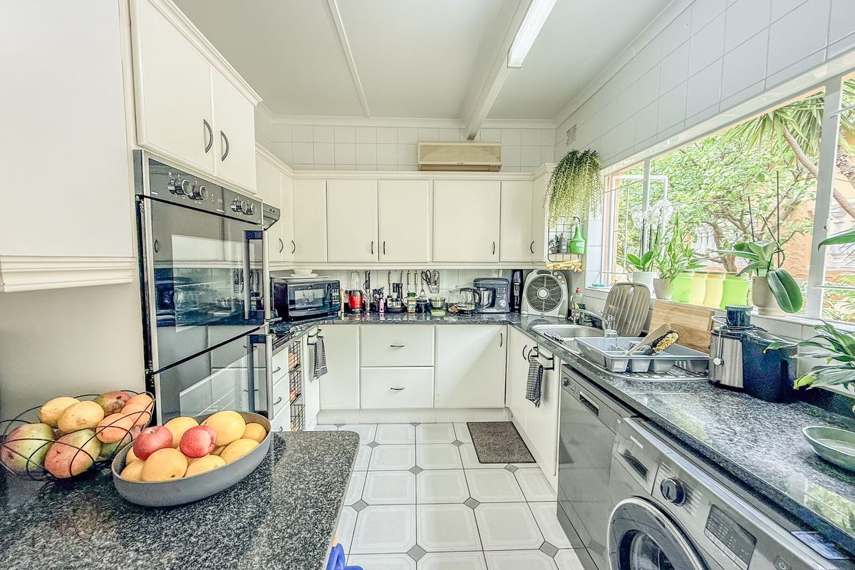 A functional kitchen featuring white cabinetry, granite countertops, a double wall oven, and integrated laundry facilities with ample natural light.