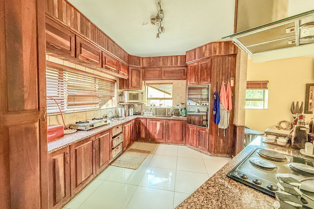 A spacious kitchen featuring extensive wooden cabinetry, granite countertops, built-in oven, and a gas hob, finished with light-colored floor tiles.
