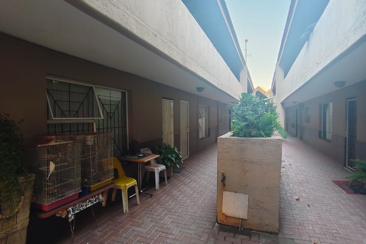 A paved exterior walkway between apartment blocks featuring a central concrete planter and external water access.