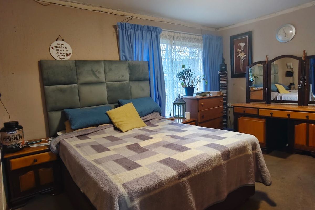 A bedroom featuring a window with a security gate and a central ceiling light fixture, requiring cosmetic updates to the wall finishes.