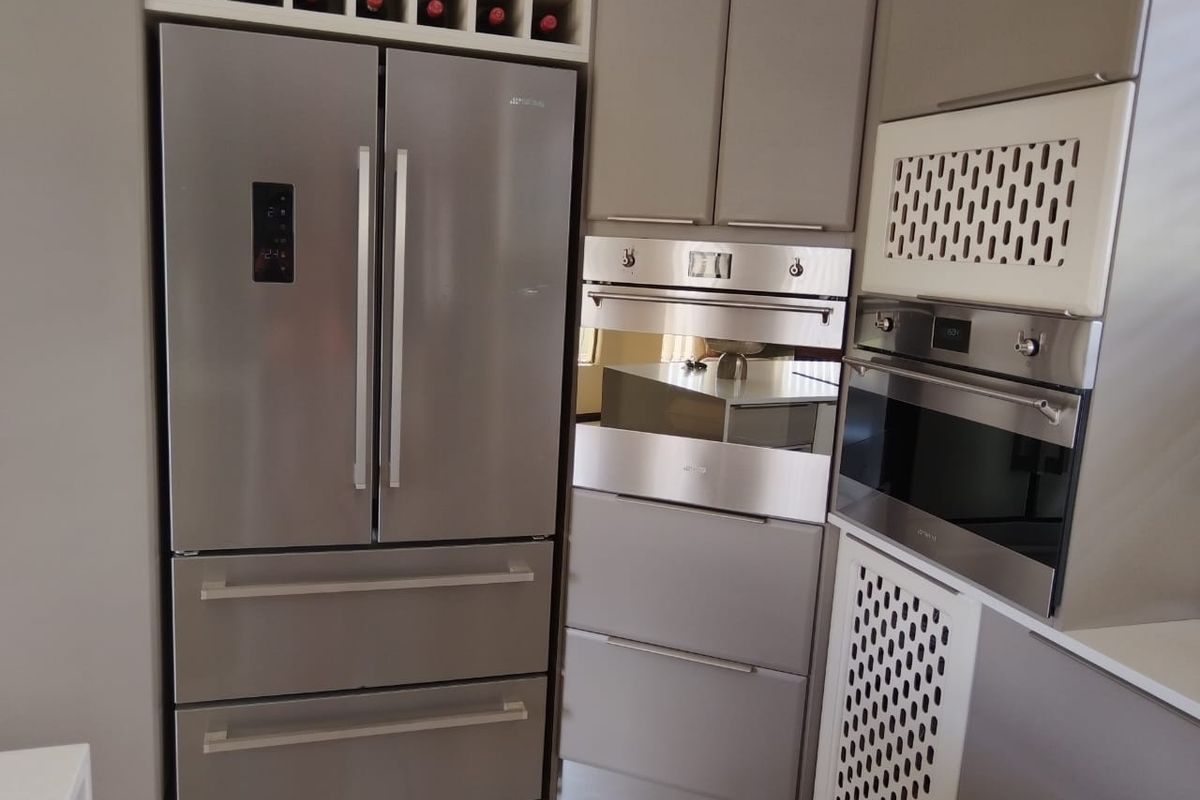 Modern kitchen featuring integrated stainless steel appliances, including a double-door refrigerator, built-in oven, and microwave, complemented by sleek grey cabinetry and wine storage.