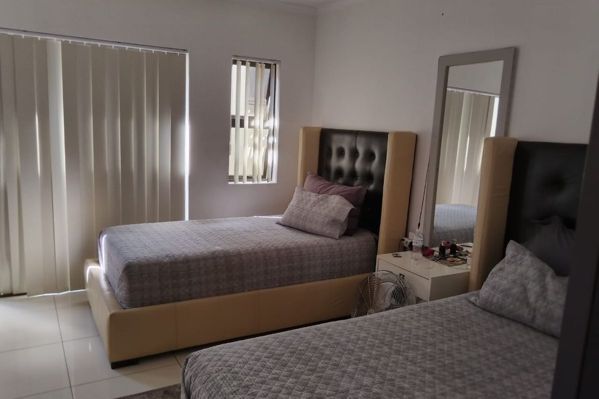 A bedroom featuring tiled flooring, vertical blinds, and a window, providing a functional and well-lit sleeping space.