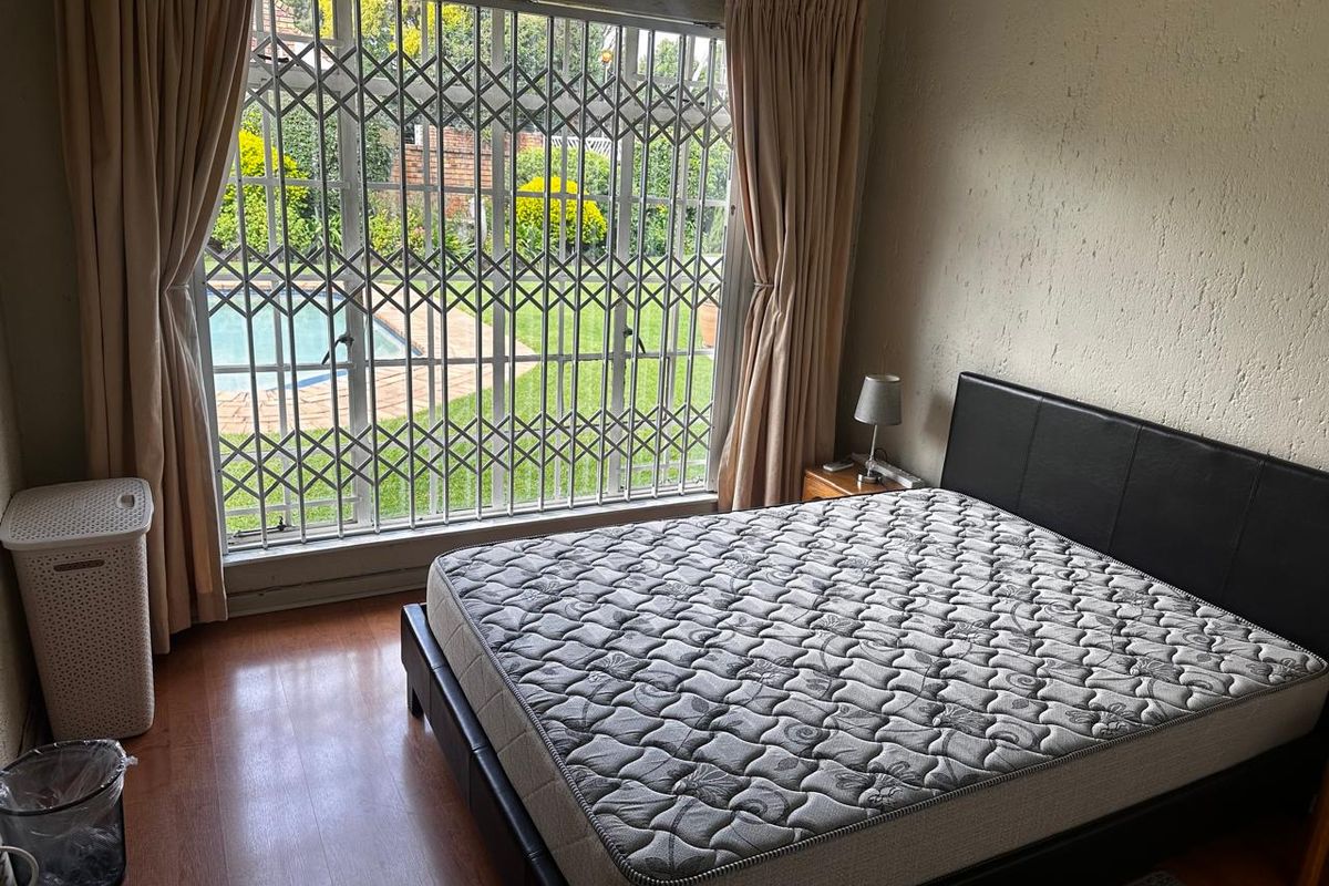 A bedroom featuring laminate flooring, large window with security gate, and direct views of the garden and swimming pool area.