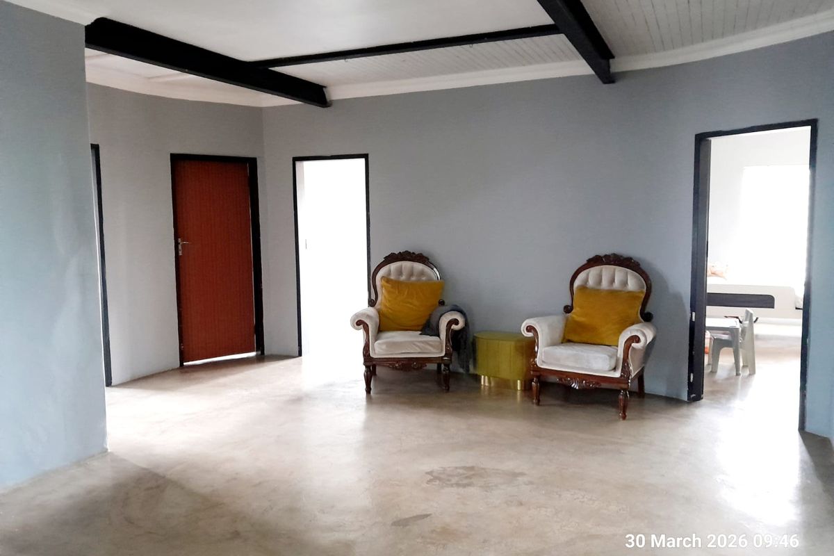 Spacious living area featuring exposed ceiling beams, smooth concrete flooring, and multiple doorways leading to adjacent rooms.