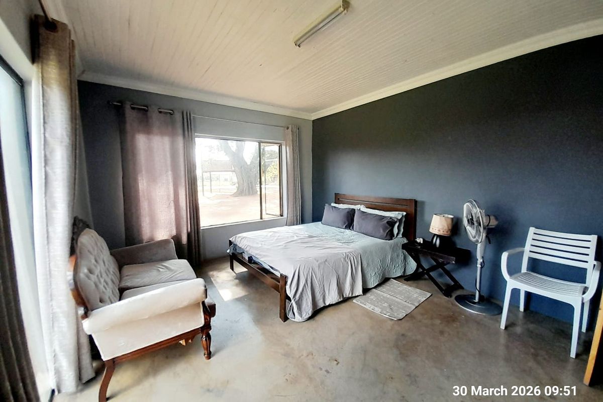 A spacious bedroom featuring concrete flooring, a dark accent wall, and large windows providing natural light and views of the farm grounds.