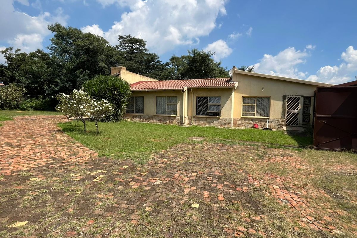 A view of the rear exterior of the house featuring a tiled roof, stone cladding accents, and a paved driveway leading to the garden.