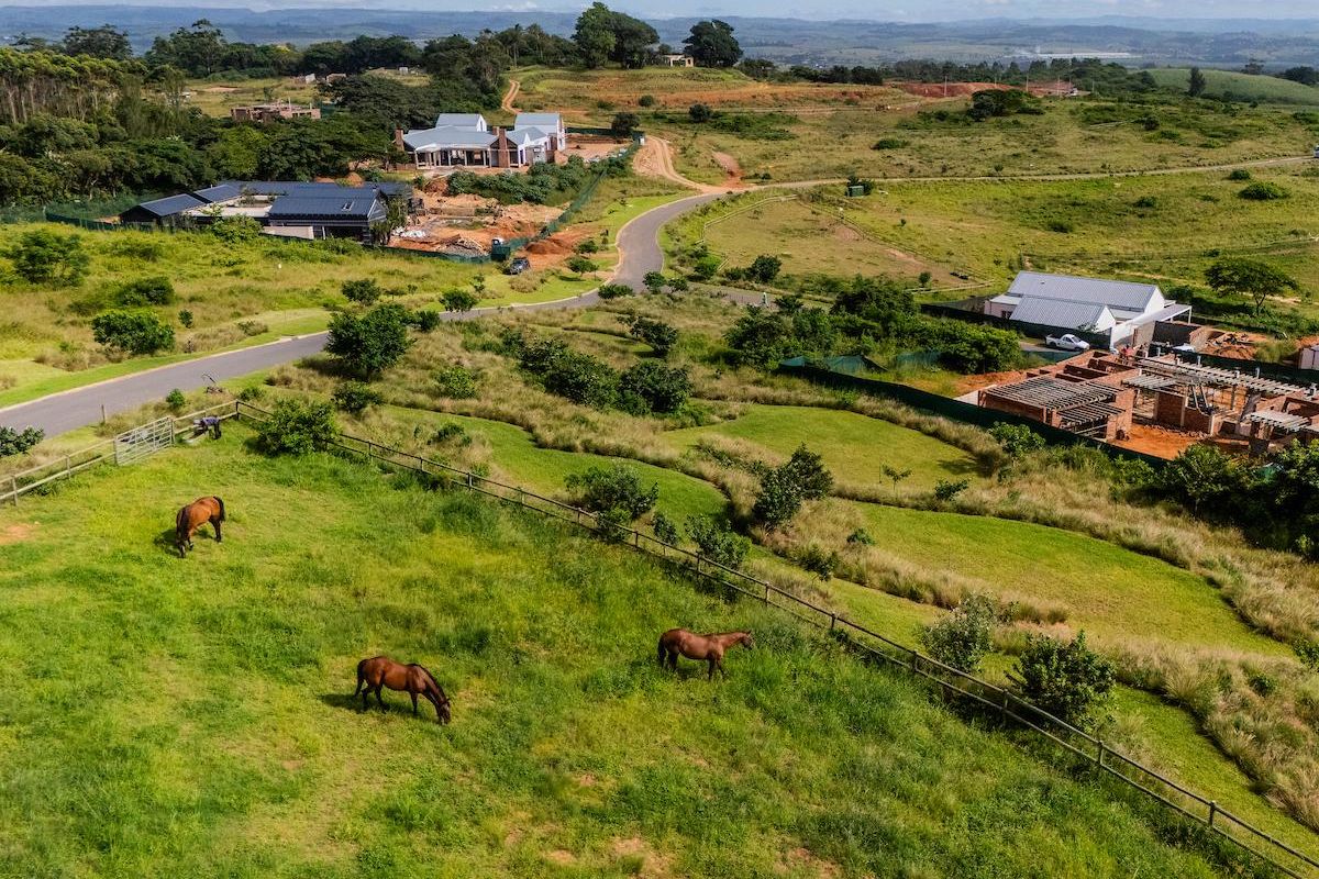 Aerial view of a residential estate featuring rolling green pastures, post-and-rail fencing, and surrounding residential development under construction.