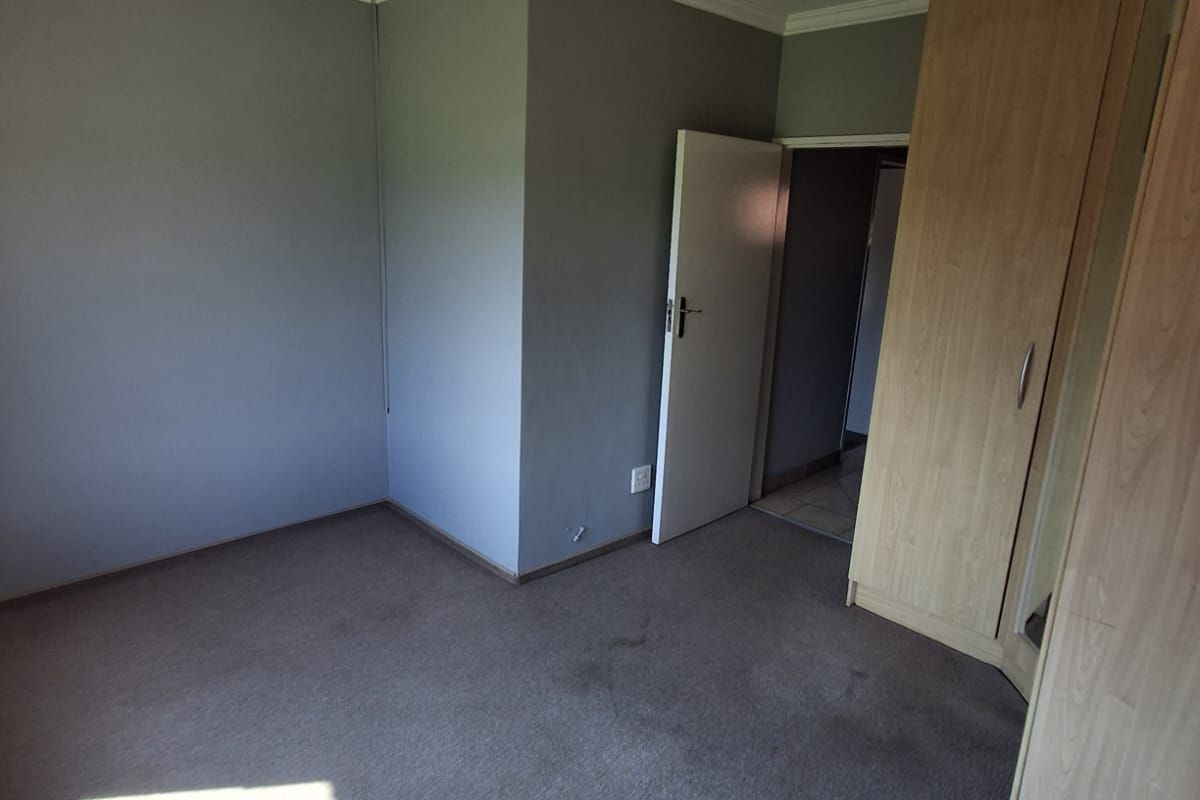 A bedroom featuring built-in wooden wardrobes, neutral grey walls, and carpeted flooring, offering a functional and versatile living space.