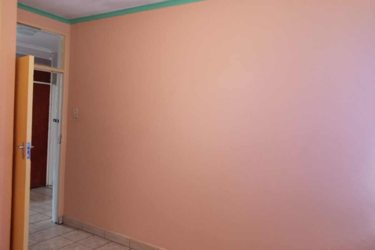 A simple, empty bedroom featuring peach-colored walls, green ceiling trim, and tiled flooring, with a doorway leading to an adjacent room.
