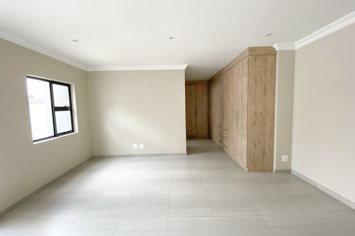 A spacious, modern bedroom featuring neutral wall tones, large format floor tiles, and extensive built-in wooden cabinetry for ample storage.