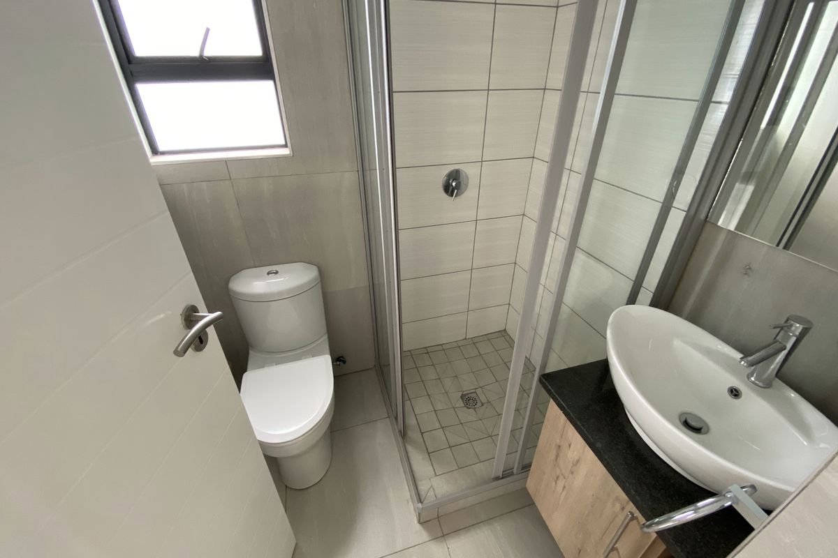 Modern bathroom featuring a glass-enclosed shower, a contemporary vanity with a vessel sink, and a white toilet, finished with neutral wall and floor tiles.