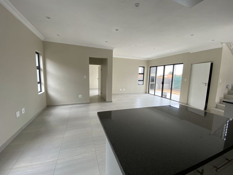 Spacious open-plan living area featuring neutral tiled flooring, recessed ceiling lighting, and large glass sliding doors leading to the exterior.