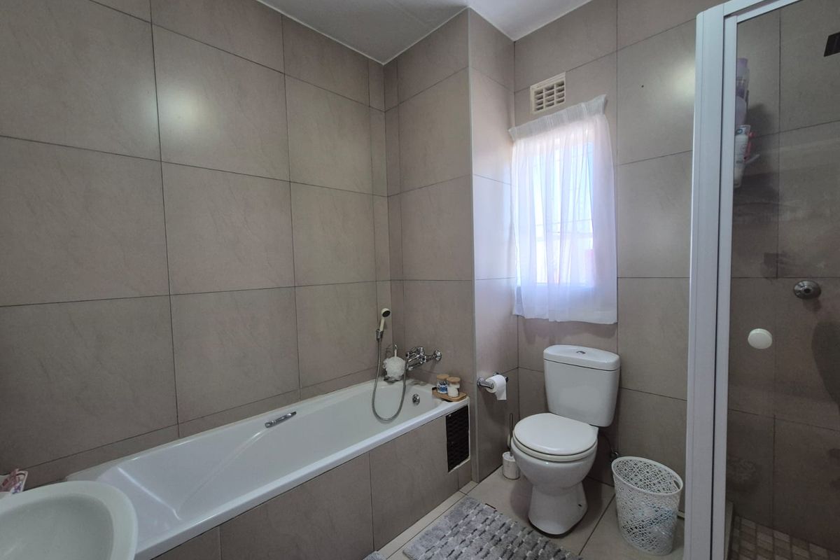 A modern bathroom featuring floor-to-ceiling neutral tiling, a built-in bathtub, a separate glass-enclosed shower, and a standard toilet.
