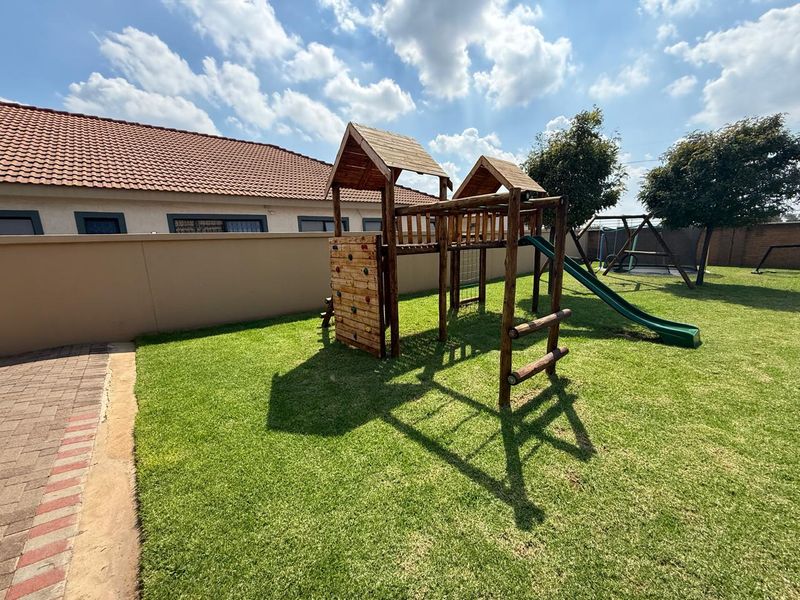 A well-maintained rear garden featuring a manicured lawn, paved walkway, and a wooden jungle gym structure.