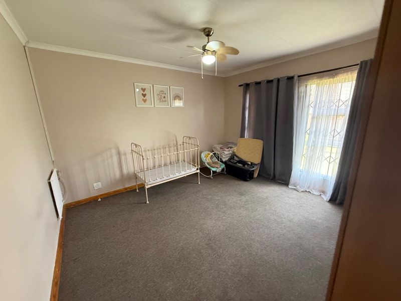 A bedroom featuring carpeted flooring, a ceiling fan, and a sliding glass door with security gate leading to the exterior.