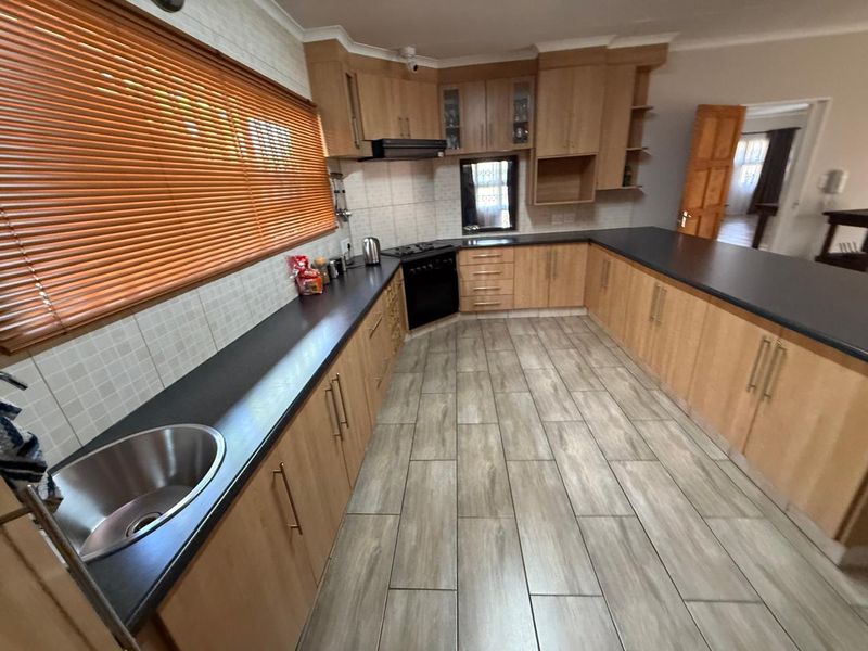 Spacious kitchen featuring light wood cabinetry, dark laminate countertops, stainless steel sink, and integrated oven with extractor fan.