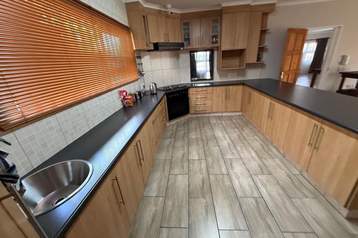 Spacious kitchen featuring light wood cabinetry, dark laminate countertops, stainless steel sink, and integrated oven with extractor fan.