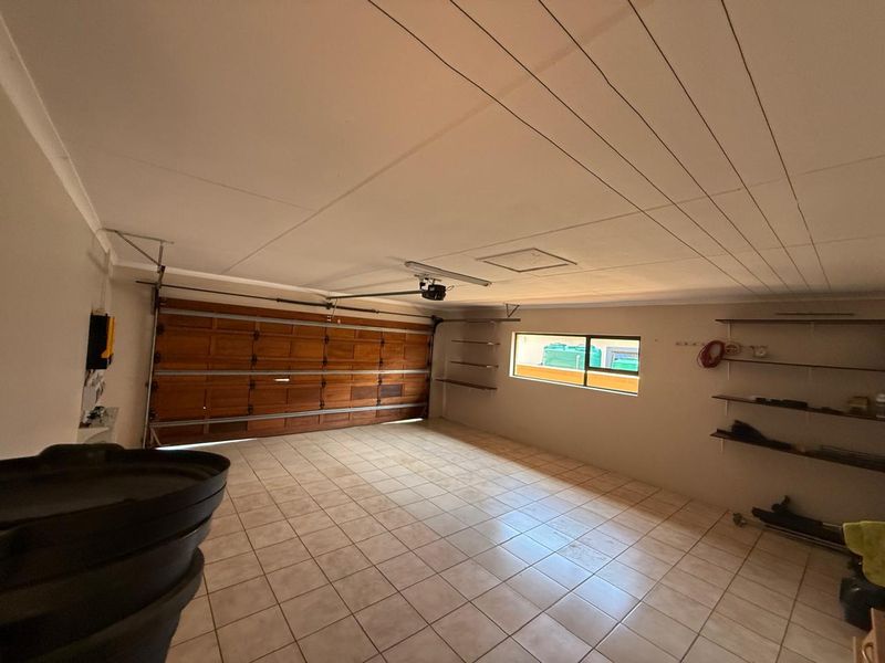 Spacious double garage featuring tiled flooring, a wooden sectional garage door, and built-in wall shelving for storage.