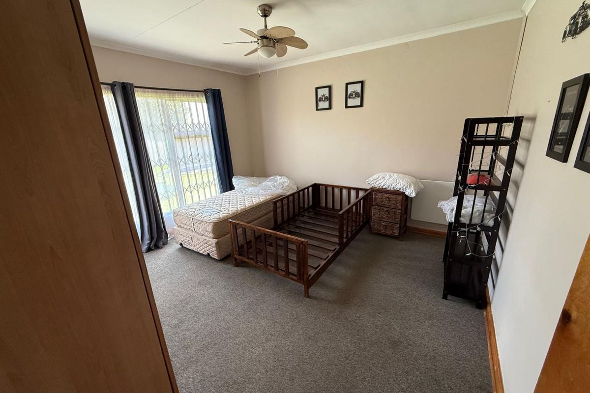 A spacious bedroom featuring neutral wall tones, carpeted flooring, a ceiling fan, and large sliding glass doors with security bars.
