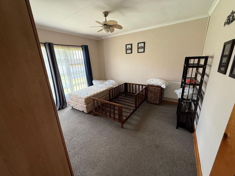 A spacious bedroom featuring neutral wall tones, carpeted flooring, a ceiling fan, and large sliding glass doors with security bars.