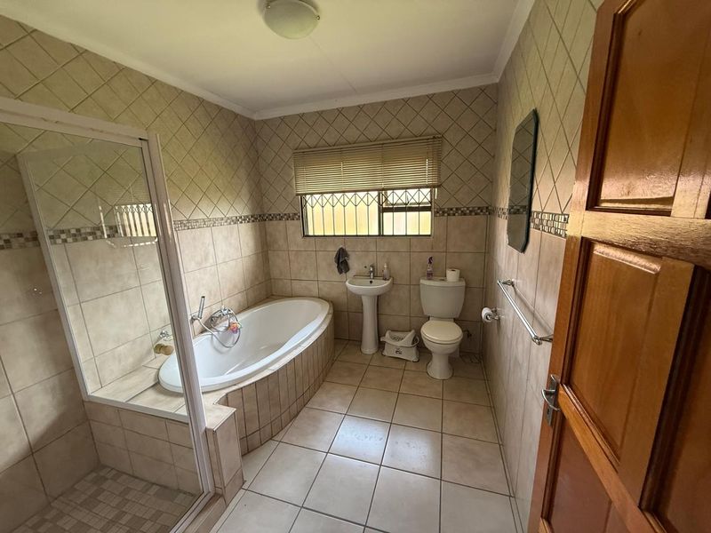 A functional bathroom featuring a built-in bathtub, separate glass-enclosed shower, pedestal basin, and toilet with neutral wall and floor tiling.