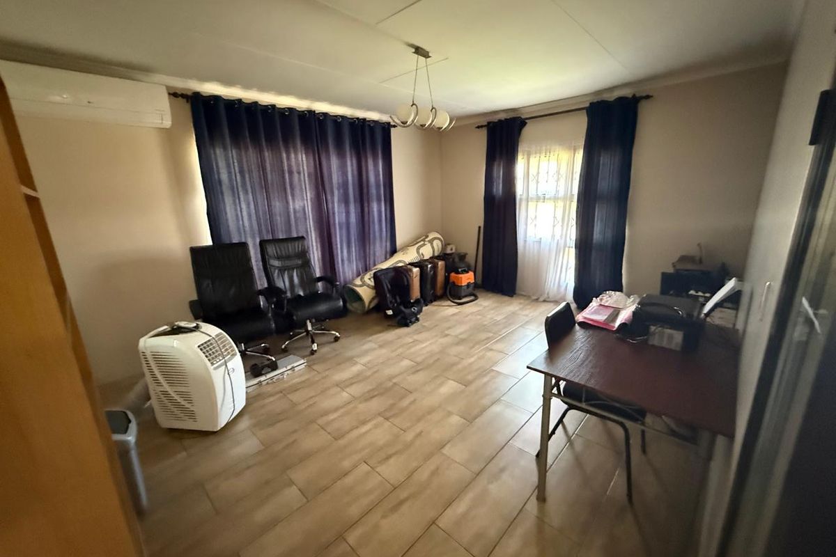A spacious living area featuring tiled flooring, a wall-mounted air conditioning unit, and large windows with curtain treatments.