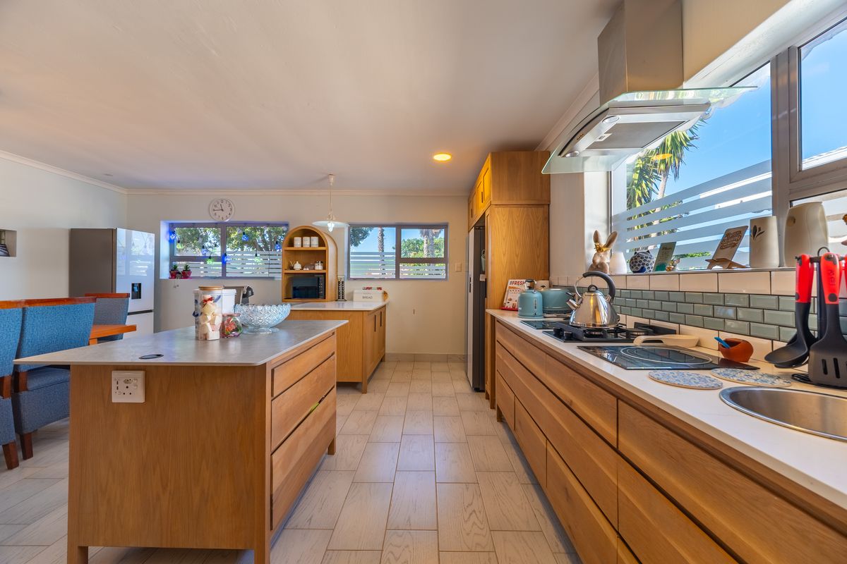A well-maintained kitchen featuring wooden cabinetry, a central island, built-in gas hob, stainless steel extractor fan, and tiled flooring with ample natural light.