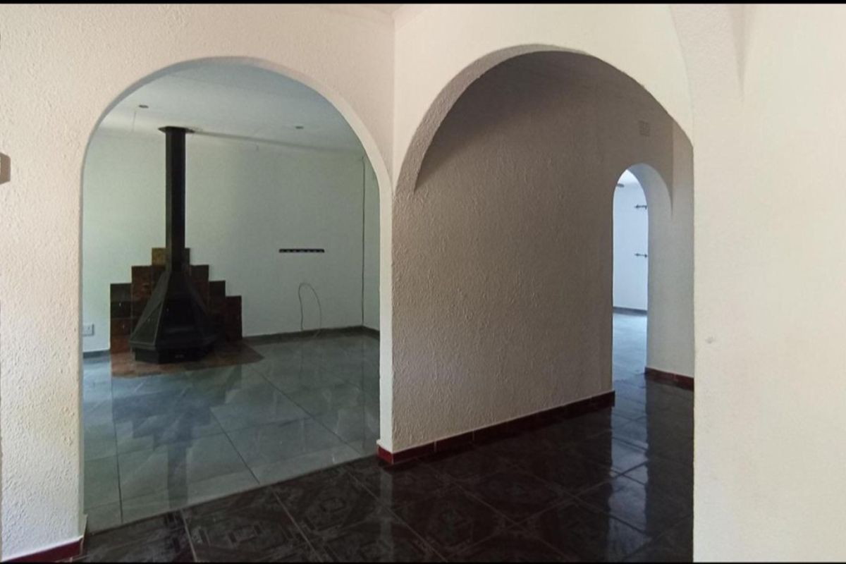 An interior view featuring arched doorways connecting living spaces, highlighted by a central freestanding fireplace and tiled flooring throughout.